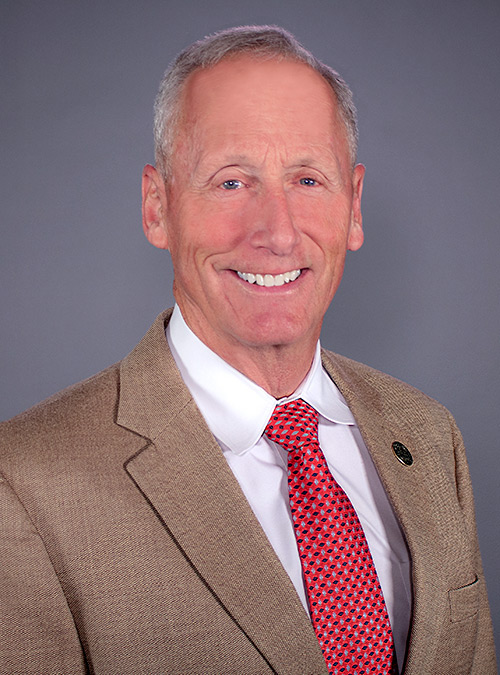 Portrait of Rick Lee wearing a tan jacket with white shirt and red tie